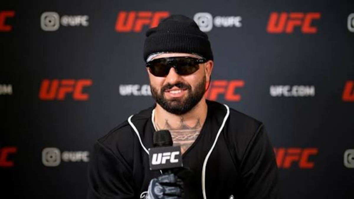 Josh Hokit in sunglasses and a beanie speaking at a UFC media day