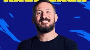 John Kavanagh, Conor McGregor's longtime coach, smiling in a black T-shirt in a Ki MMA promotional graphic