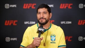Alex Pereira in a yellow Brazil jersey speaking into a UFC microphone during a UFC.com interview