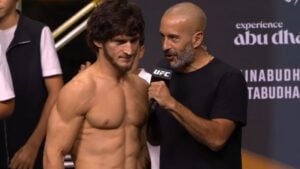 Jon Anik speaks into a UFC microphone beside Movsar Evloev on stage in Abu Dhabi ahead of UFC 333