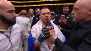 Petr Yan, draped in a Russian flag, speaks into a UFC microphone during a post-fight interview in the Octagon