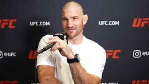 Sean Strickland speaks into a microphone in front of a UFC backdrop at a media session
